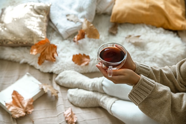 Accogliente autunno a casa, una donna con un libro e un tè a riposo. Uno stile di vita accogliente. Parti del corpo nella composizione.