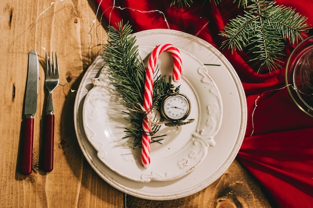 Accogliente bella tavola di Capodanno con una tovaglia rossa, utensili antichi e un orologio vintage sul tavolo.