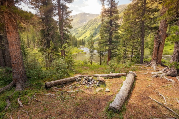 Accogliente campeggio con caminetto e tronchi di legno per sedersi Maestose montagne e fiume sullo sfondo