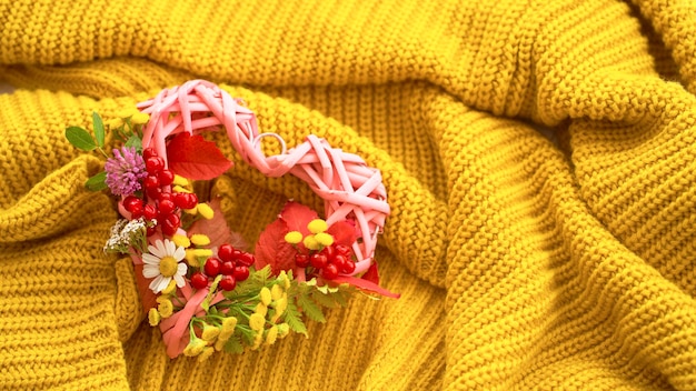 Accogliente composizione autunnale. Sciarpa in maglia, cuore di foglie e fiori autunnali