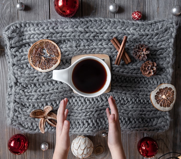 Accogliente composizione domestica con una tazza di tè, mani del bambino, elemento a maglia, dettagli di decorazioni natalizie, posa piatta.