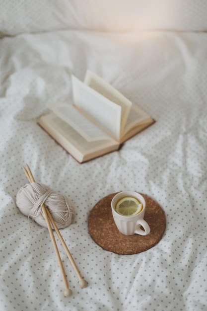 Accogliente composizione invernale con un libro di tè al limone e ferri da maglia sulle lenzuola