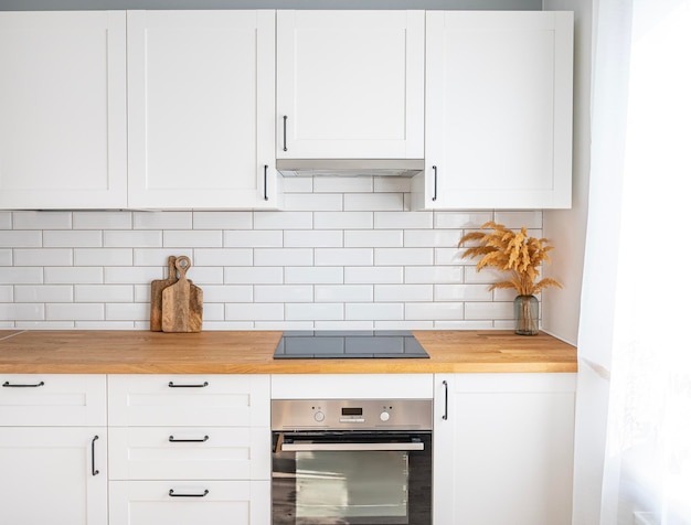 Accogliente cucina bianca con fiori da appoggio in legno e taglieri in un interno minimalista con luce solare durante il giorno