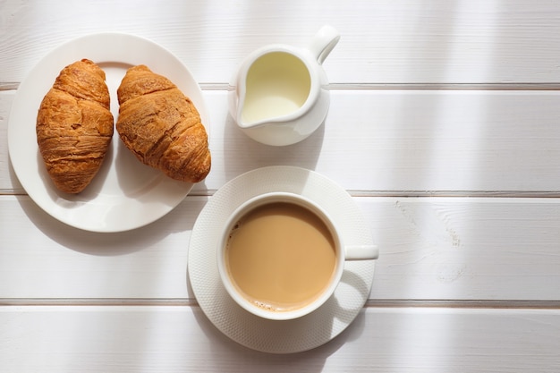 Accogliente mattina piatta Tazza di caffè con latte e due croissant su un piatto su un tavolo di legno bianco white