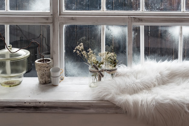 Accogliente natura morta invernale. Piante secche, tazzine da caffè e pelliccia calda sul davanzale della cucina vintage. Stagione invernale, trascorrere il periodo invernale al concetto di casa accogliente.