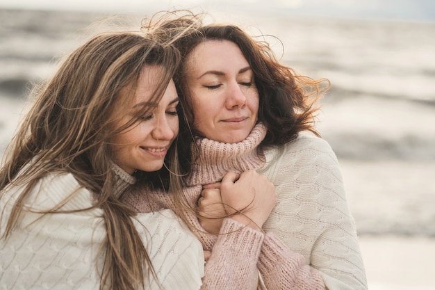 Accogliente passeggiata autunnale di due ragazze sulla riva del mare ventoso, sorelle adulte stanno trarking in coperte f...