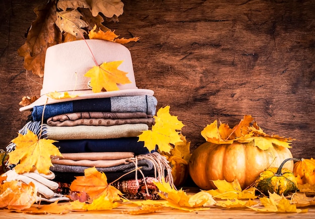 Accogliente sfondo autunnale con caldi abiti autunnali e invernali sciarpe maglioni cappello di feltro guanti zucche foglie cadute su fondo di legno rustico