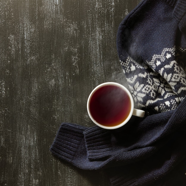 Accogliente sfondo casa invernale, tazza di tè caldo e caldo maglione lavorato a maglia sulla tavola nera.