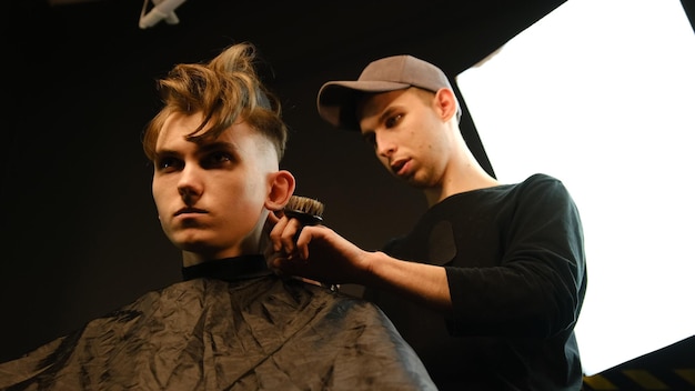 Acconciatura e taglio di capelli da uomo con tagliacapelli in un negozio di barbiere o parrucchiere Servizio di parrucchiere in un moderno negozio di barbiere in un lampo scuro con luce calda vista ad angolo basso