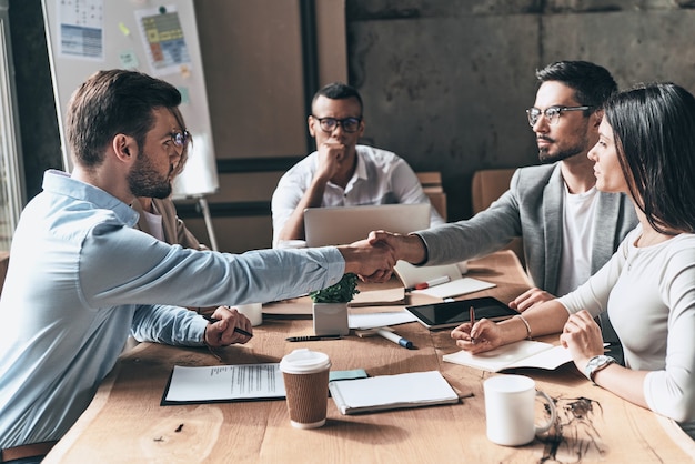 Accordo. Giovani uomini moderni in abbigliamento casual intelligente che si stringono la mano mentre lavorano nell'ufficio creativo