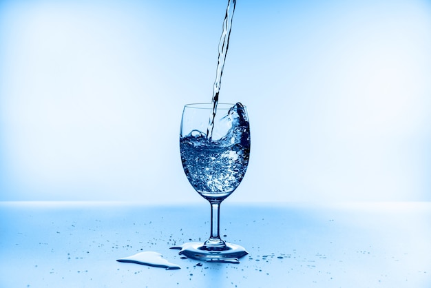 Accumulazione della spruzzata dell'acqua nel bicchiere di vino isolato sulla parete blu