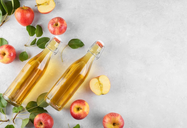 Aceto di sidro di mele in due bottiglie di vetro e mele fresche con foglie su sfondo chiaro vista dall'alto spazio copia