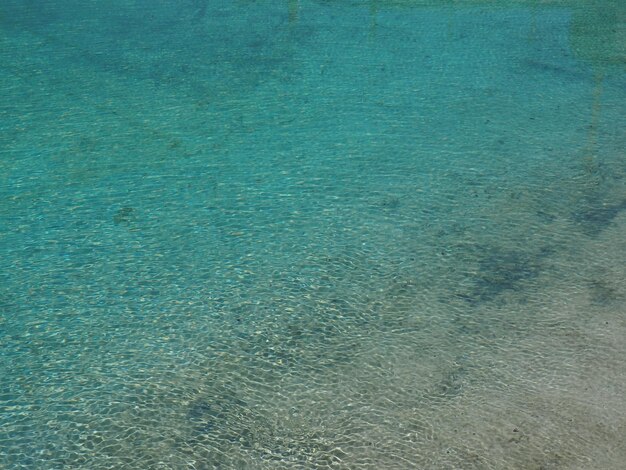 Acqua blu e turchese Acqua di mare limpida con onde e riverbero del sole Il fondale è visibile