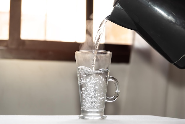 Acqua bollente gorgogliante che cade in una tazza trasparente per la colazione