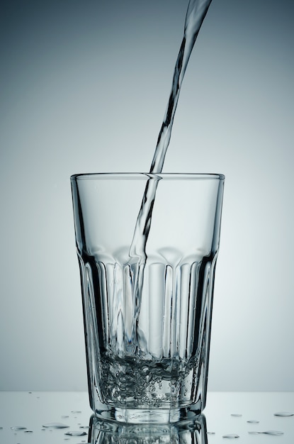 Acqua che versa in vetro, isolato su bianco