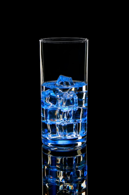 Acqua con ghiaccio in un bicchiere con un bagliore blu. Cocktail rinfrescante sul nero