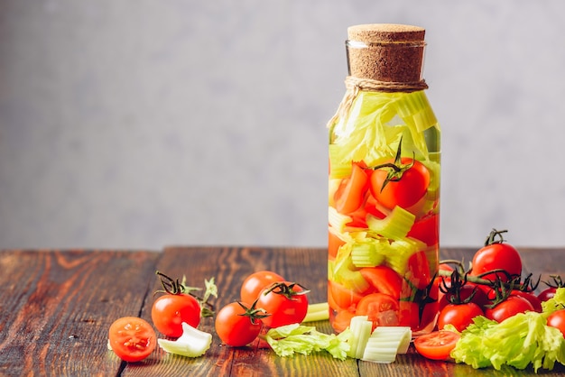 Acqua detergente infusa con gambi di sedano e pomodorini. Ingredienti sparsi sulla tavola di legno. Copia spazio a sinistra.