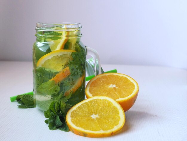 Acqua detox con arance e menta in una tazza Arance fresche tagliate e foglie di menta