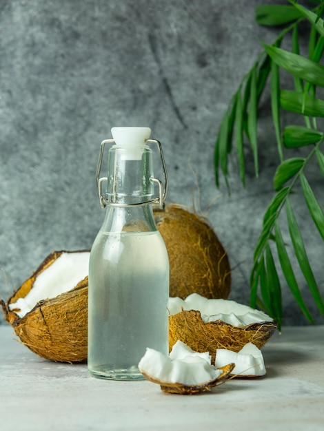 Acqua di cocco fresca e rinfrescante in una bottiglia con una noce di cocco aperta con polpa bianca su uno sfondo di cemento