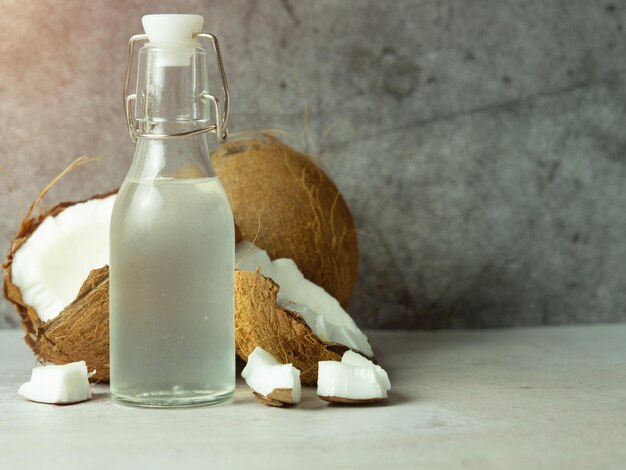 Acqua di cocco fresca e rinfrescante in una bottiglia con una noce di cocco aperta con polpa bianca su uno sfondo di cemento