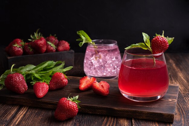 Acqua di frutta, limonata alla fragola con rametto di menta con fragole su uno sfondo di legno, concetto di bevande rinfrescanti estive, primo piano.