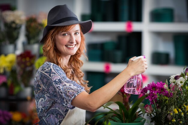 Acqua di spruzzatura sorridente del fiorista sui fiori nel negozio di fiore