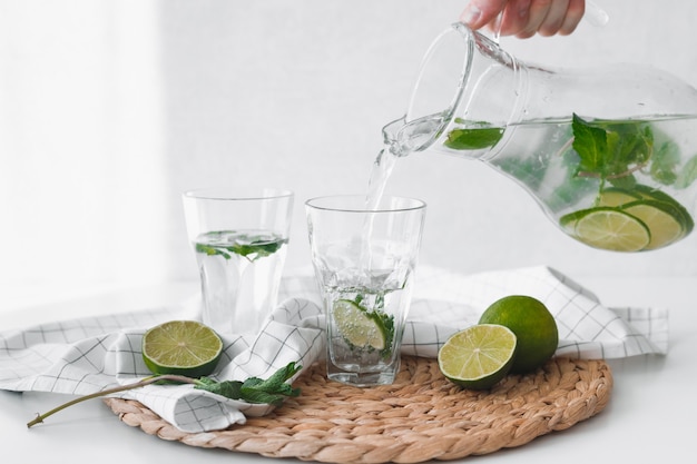 Acqua disintossicante con frutti di lime. Mano versando acqua di frutta calce dalla brocca in bicchieri.