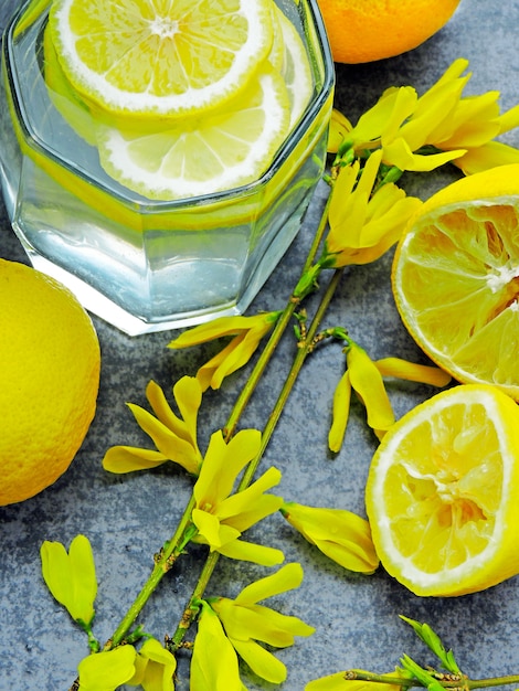 Acqua disintossicante con succo di limone e fiori gialli sui rami.