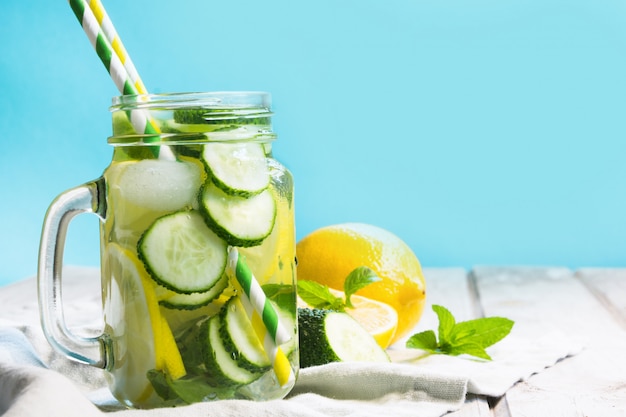 Acqua dolce di estate con il limone, il cetriolo, il ghiaccio e la menta in barattolo di muratore su un fondo di legno.