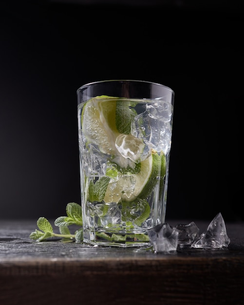 Acqua fredda fresca con lime, menta e ghiaccio in un bicchiere su sfondo di pietra scura