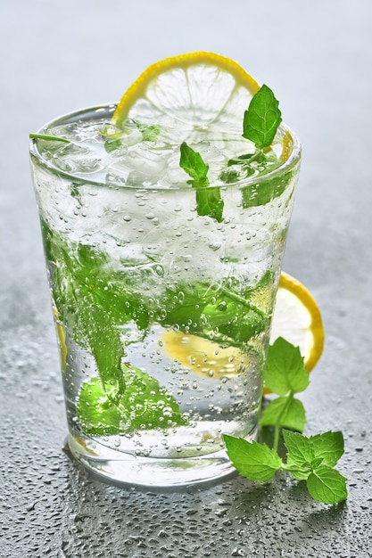 Acqua frizzante con limone e menta in vetro su una pietra grigia