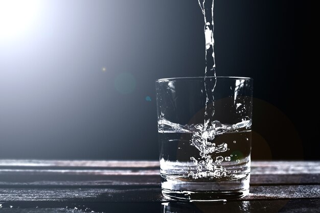 Acqua in un bicchiere, isolato su uno sfondo nero con spruzzi