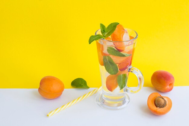 Acqua infusa con albicocca e menta nel bicchiere su sfondo giallo Spazio di copia Closeup