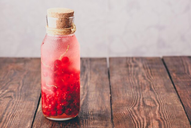 Acqua infusa di ribes rosso con ghiaccio in bottiglia di vetro