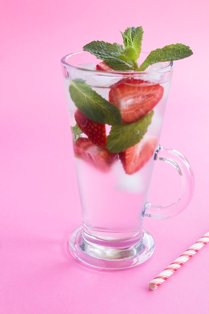 Acqua infusa o disintossicante con fragola, ghiaccio e menta nel bicchiere su sfondo rosa. Avvicinamento. Posizione verticale.