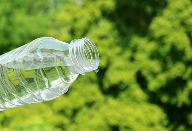 Acqua minerale del primo piano che cade dalla bottiglia di plastica con fogliame verde