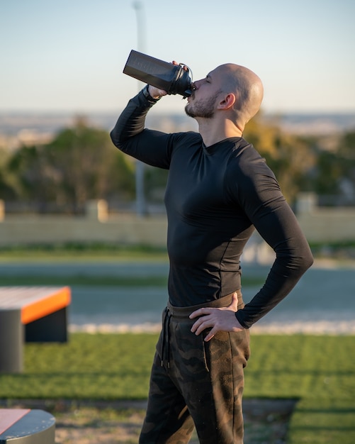 Acqua potabile del giovane uomo ispanico dopo aver lavorato nel campo sportivo