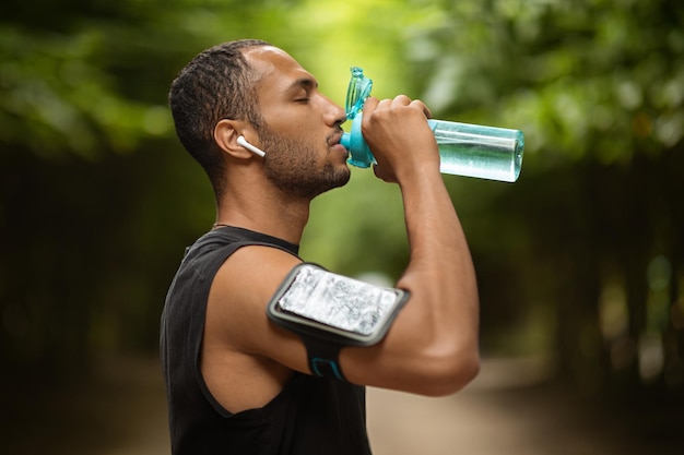 Acqua potabile dell'uomo afroamericano sportivo che si esercita all'aperto