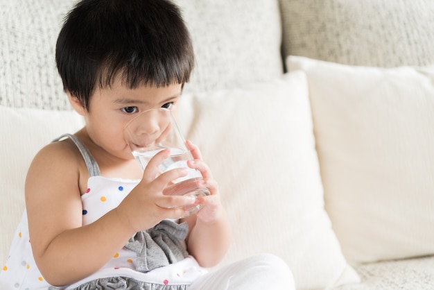 Acqua potabile della bambina sveglia sul sofà a casa. Concetto di assistenza sanitaria.