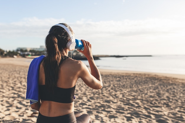 Acqua potabile della bella donna di forma fisica dopo l'allenamento davanti alla spiaggia