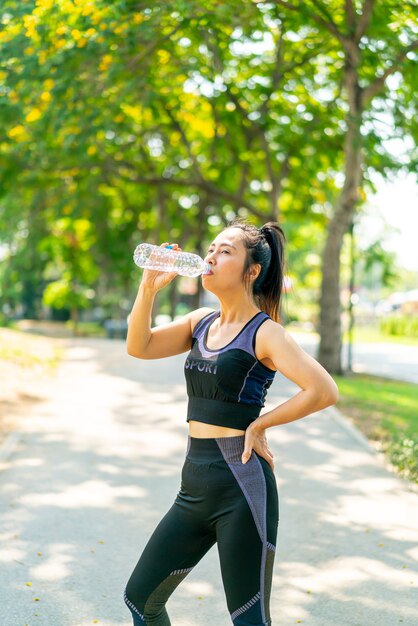 Acqua potabile della donna asiatica in abbigliamento sportivo dopo l'esercizio al parco
