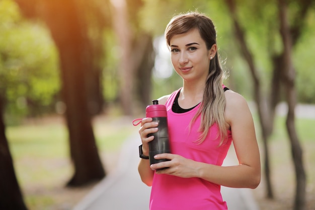 Acqua potabile della donna del corridore dell'atleta di bella forma fisica nel parco. Bottiglia d'acqua