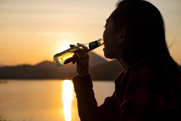 Acqua potabile della donna della siluetta sulla spiaggia al crepuscolo