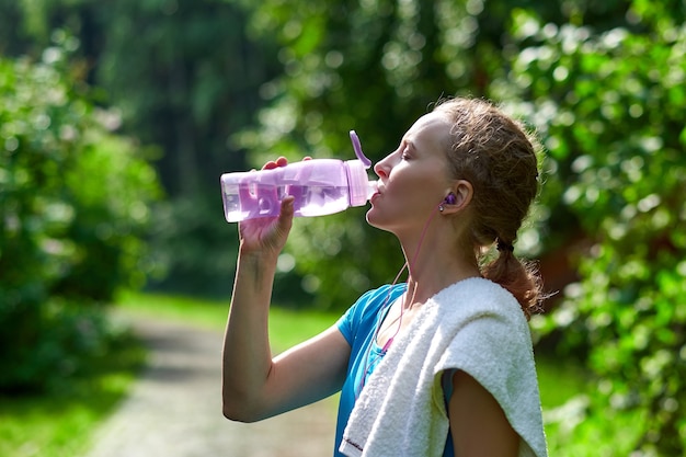 Acqua potabile della donna di forma fisica dopo l'allenamento in esecuzione nel parco estivo.