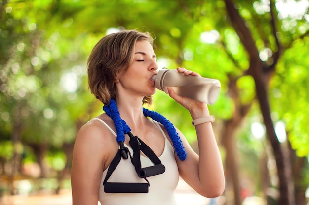 Acqua potabile della donna di sport nel parco. Concetto di fitness e assistenza sanitaria