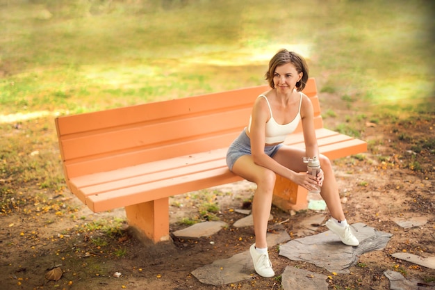 Acqua potabile della donna di sport nel parco. Concetto di fitness e assistenza sanitaria