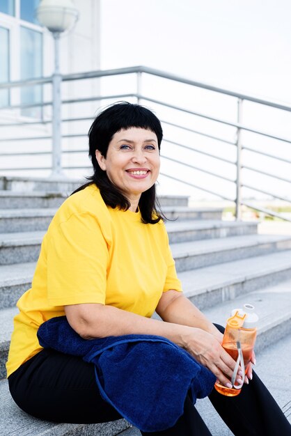 Acqua potabile della donna maggiore sorridente dopo l'allenamento all'aperto