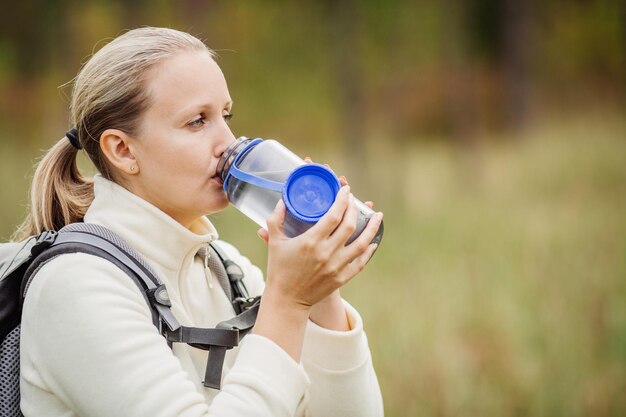 Acqua potabile della giovane donna con lo zaino alla valle della foresta