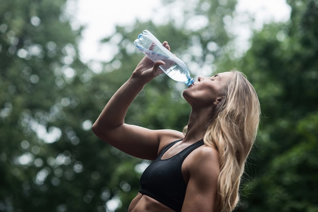 Acqua potabile della ragazza muscolare atletica dopo l&#39;allenamento Il concetto di uno stile di vita sano