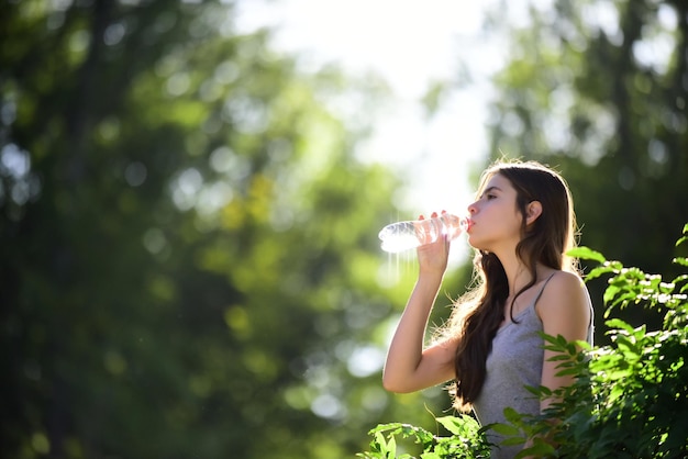 Acqua potabile sana della donna dal concetto di idratazione del soggiorno della bottiglia unità non idratata con la natura all'aperto